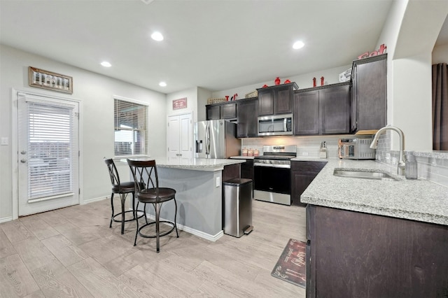 kitchen featuring a center island, sink, light wood-type flooring, appliances with stainless steel finishes, and light stone counters