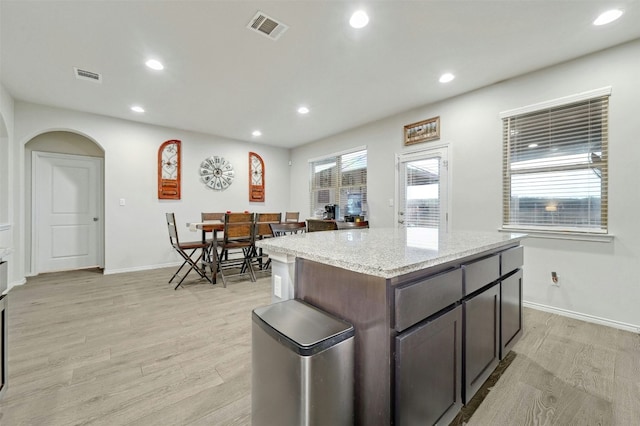 kitchen with dark brown cabinetry, light stone counters, a center island, and light hardwood / wood-style floors