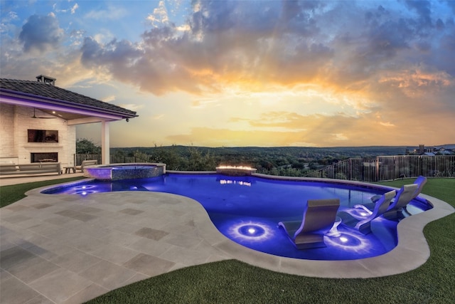 pool at dusk with an in ground hot tub, a patio area, and an outdoor fireplace