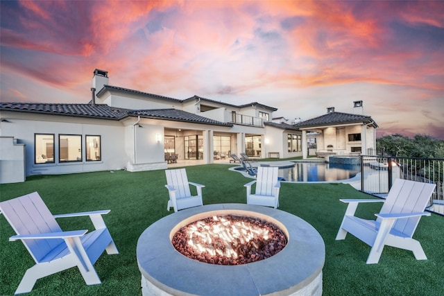 back house at dusk featuring a yard, a balcony, an outdoor fire pit, and a patio area