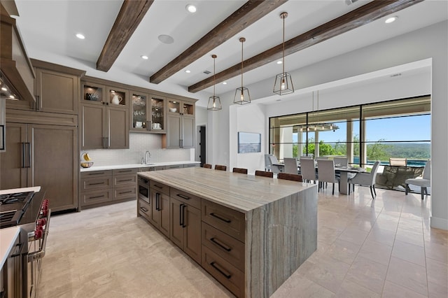 kitchen with light stone countertops, decorative backsplash, beam ceiling, hanging light fixtures, and a large island