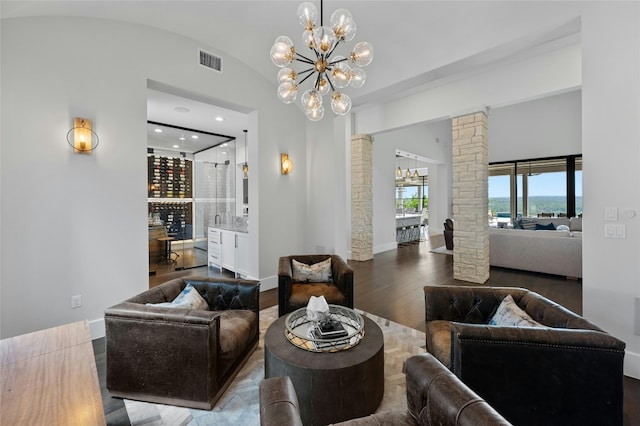 living room with hardwood / wood-style floors, a notable chandelier, vaulted ceiling, and decorative columns