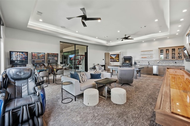 living room with a raised ceiling, ceiling fan, and carpet flooring