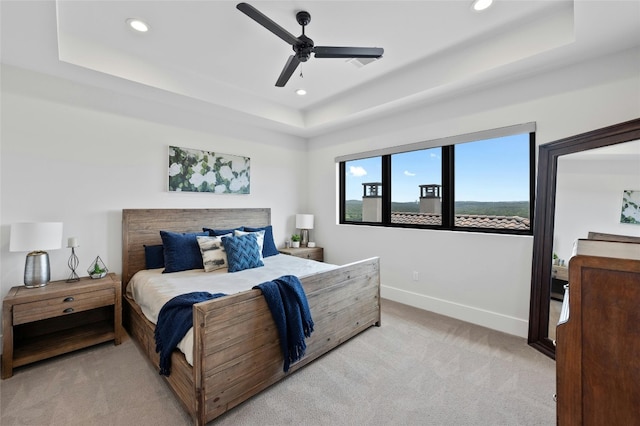 carpeted bedroom with a raised ceiling and ceiling fan