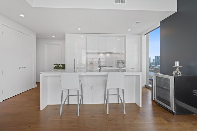 kitchen with a kitchen breakfast bar, wine cooler, tasteful backsplash, dark hardwood / wood-style floors, and white cabinets