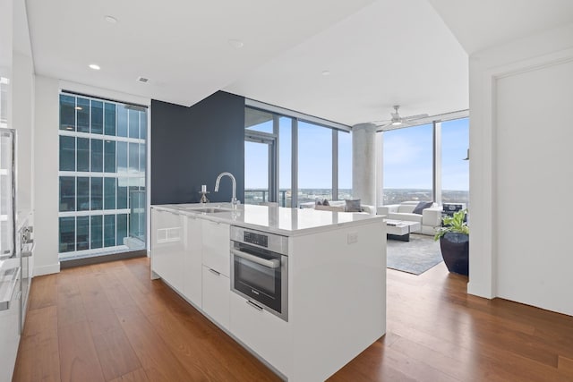 kitchen featuring floor to ceiling windows, stainless steel oven, white cabinets, dark hardwood / wood-style floors, and an island with sink