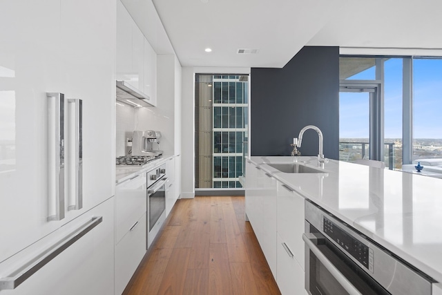 kitchen featuring white cabinetry, sink, backsplash, appliances with stainless steel finishes, and hardwood / wood-style flooring