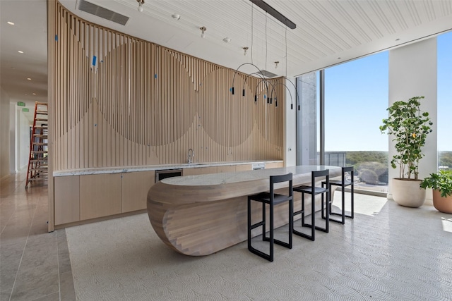 interior space featuring light brown cabinetry, expansive windows, beverage cooler, sink, and hanging light fixtures