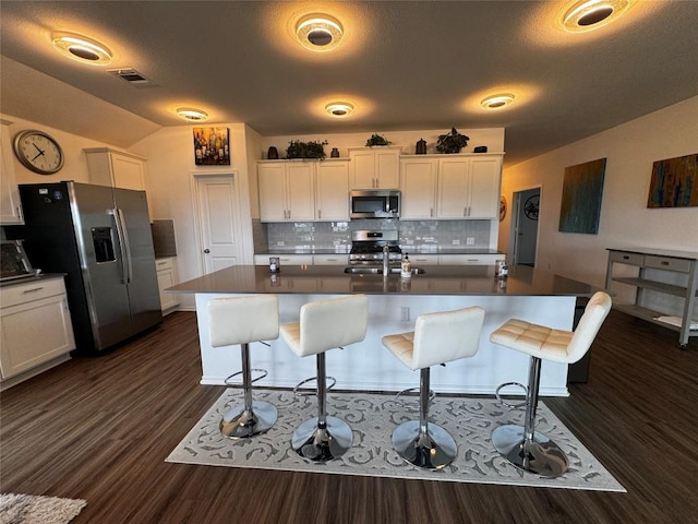 kitchen featuring dark countertops, white cabinetry, appliances with stainless steel finishes, and a kitchen breakfast bar