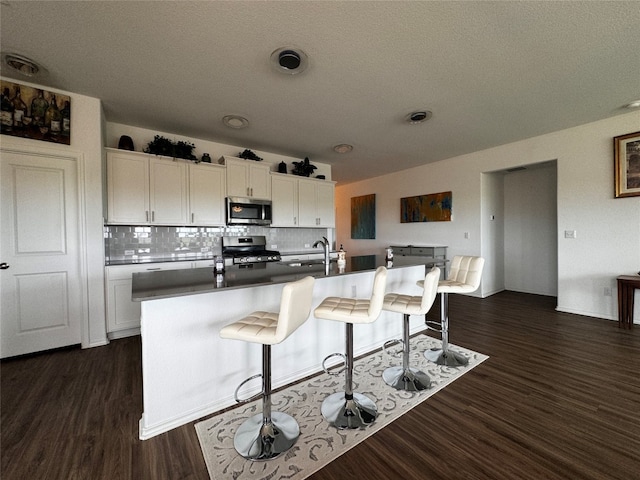 kitchen featuring white cabinets, dark wood-style floors, a breakfast bar area, and stainless steel appliances