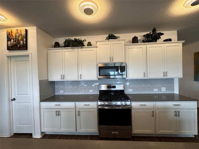 kitchen with appliances with stainless steel finishes, dark countertops, backsplash, and white cabinetry