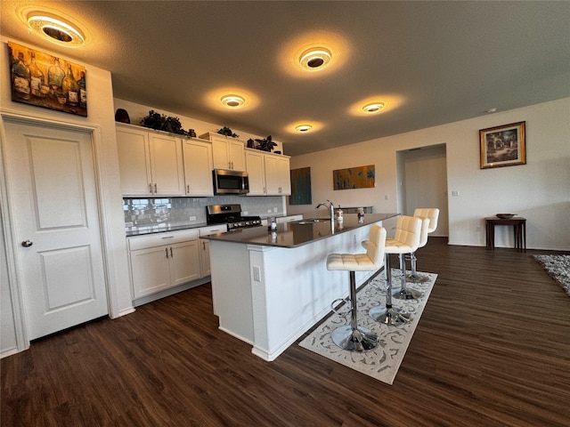 kitchen with stainless steel appliances, a sink, white cabinetry, a kitchen breakfast bar, and a center island with sink