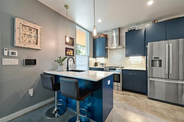 kitchen with appliances with stainless steel finishes, a kitchen breakfast bar, wall chimney exhaust hood, blue cabinetry, and hanging light fixtures