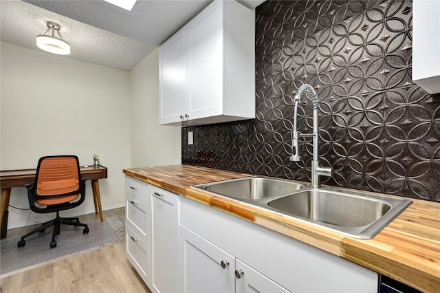 kitchen with backsplash, wooden counters, a textured ceiling, light hardwood / wood-style floors, and white cabinetry