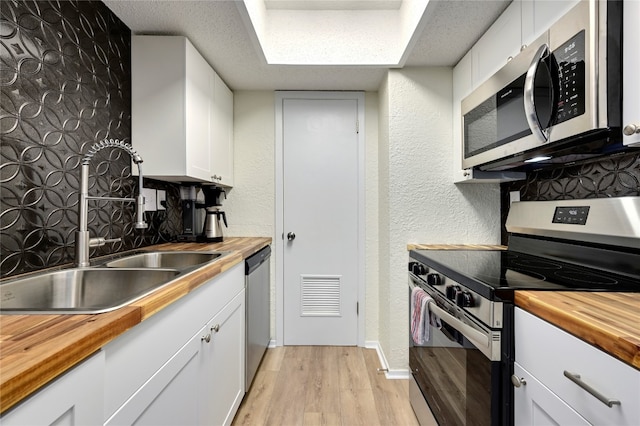 kitchen with white cabinets, light wood-type flooring, stainless steel appliances, and wood counters