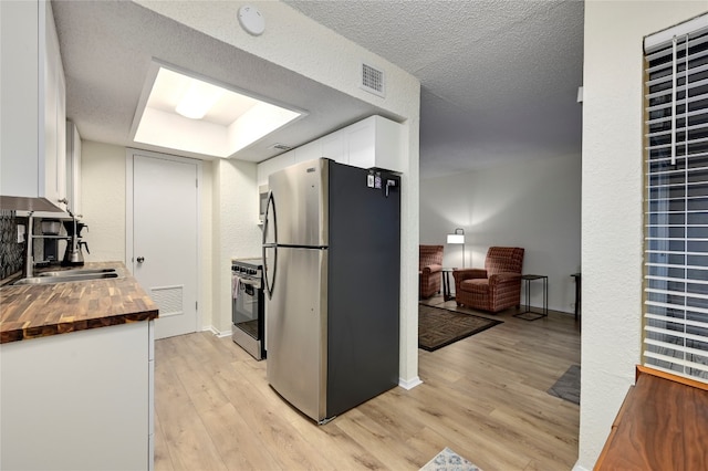 kitchen with wood counters, white cabinets, light wood-type flooring, a textured ceiling, and stainless steel appliances