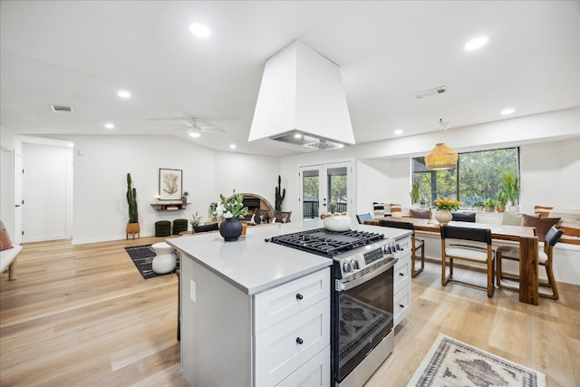 kitchen with stainless steel gas range oven, white cabinets, hanging light fixtures, ceiling fan, and light wood-type flooring