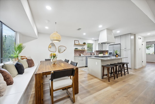 kitchen with pendant lighting, a kitchen breakfast bar, light hardwood / wood-style flooring, custom range hood, and stainless steel appliances