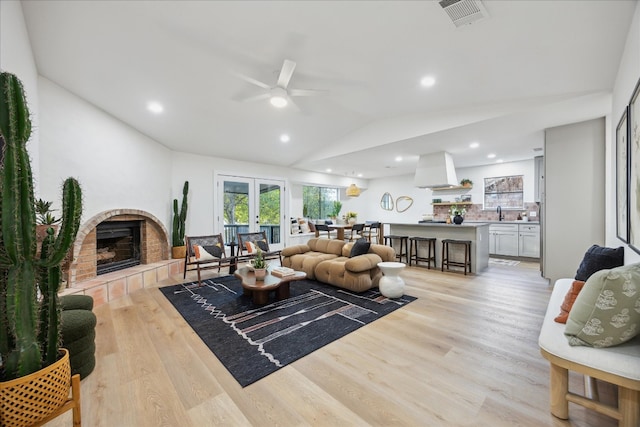 living room featuring ceiling fan, light hardwood / wood-style flooring, a tile fireplace, and vaulted ceiling