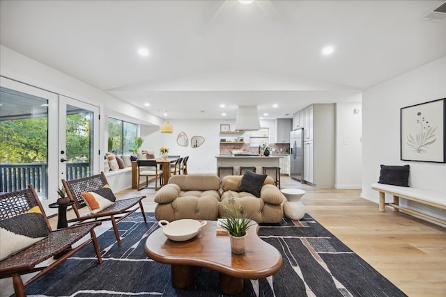 living room featuring french doors, light wood-type flooring, and vaulted ceiling