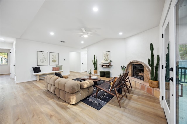 living room featuring a tiled fireplace, ceiling fan, light hardwood / wood-style floors, and vaulted ceiling