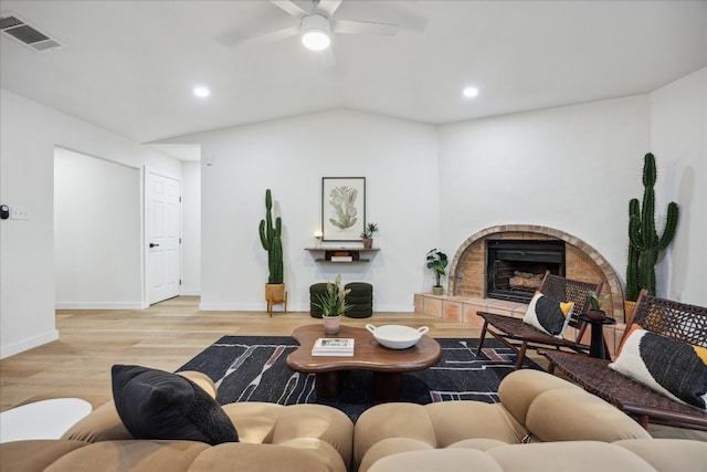 living room featuring ceiling fan, light hardwood / wood-style floors, lofted ceiling, and a brick fireplace