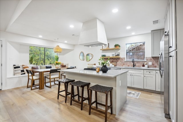 kitchen featuring premium range hood, sink, a kitchen island, and light hardwood / wood-style floors