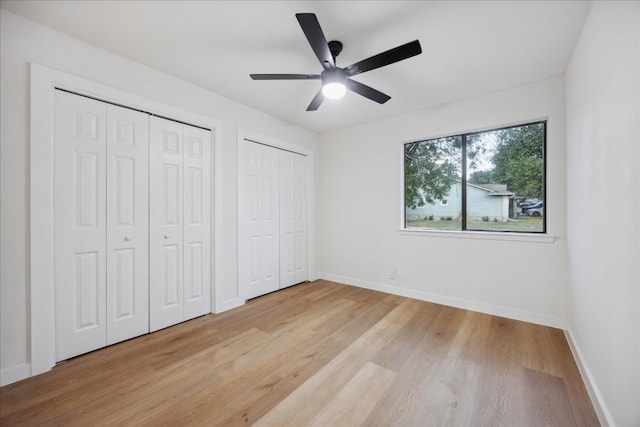 unfurnished bedroom featuring light hardwood / wood-style floors, ceiling fan, and multiple closets