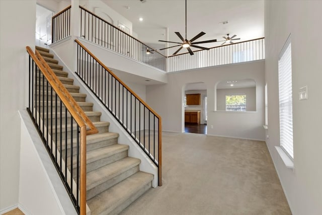 stairs featuring carpet flooring, ceiling fan, and a towering ceiling