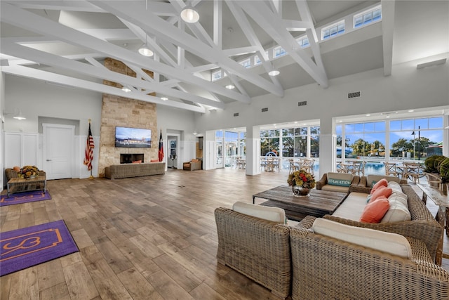 interior space featuring wood-type flooring, high vaulted ceiling, a stone fireplace, and beam ceiling