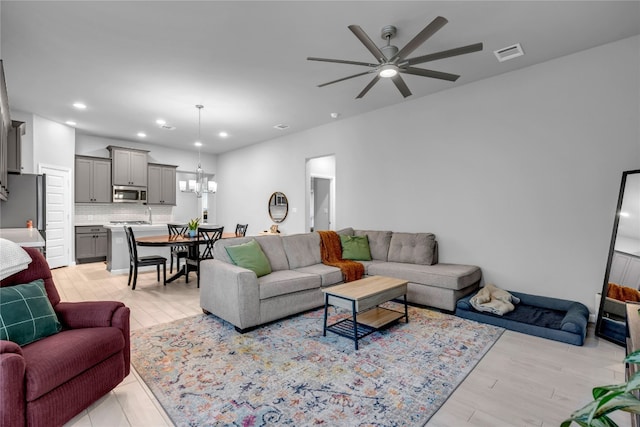 living room with ceiling fan with notable chandelier and light wood-type flooring