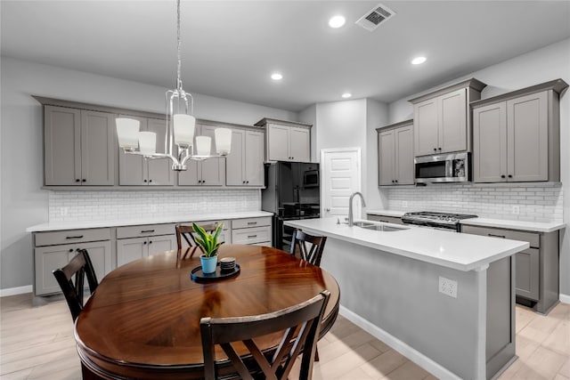 kitchen with a kitchen island with sink, sink, gray cabinets, appliances with stainless steel finishes, and decorative light fixtures