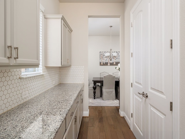 interior space featuring backsplash, a notable chandelier, decorative light fixtures, dark hardwood / wood-style flooring, and light stone countertops