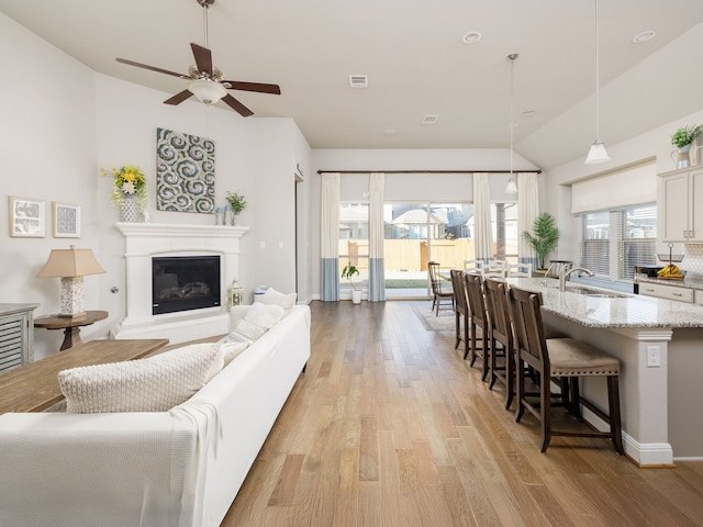 living room with ceiling fan, light wood-type flooring, sink, and lofted ceiling