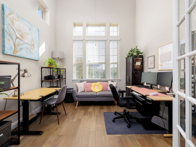 office space with light hardwood / wood-style floors, french doors, and a towering ceiling