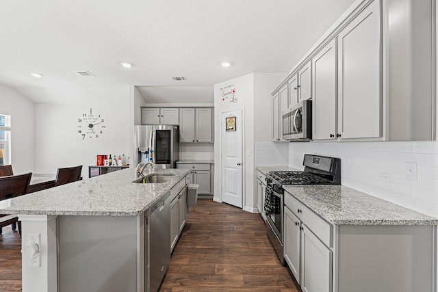 kitchen with light stone countertops, an island with sink, dark hardwood / wood-style floors, and appliances with stainless steel finishes