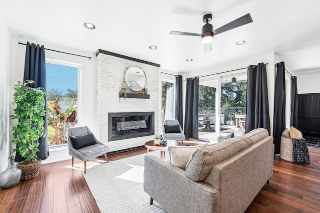 living room featuring dark wood-type flooring, a wealth of natural light, a large fireplace, and ceiling fan