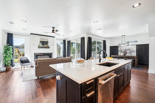 kitchen featuring a fireplace, dishwasher, sink, dark hardwood / wood-style flooring, and a center island with sink