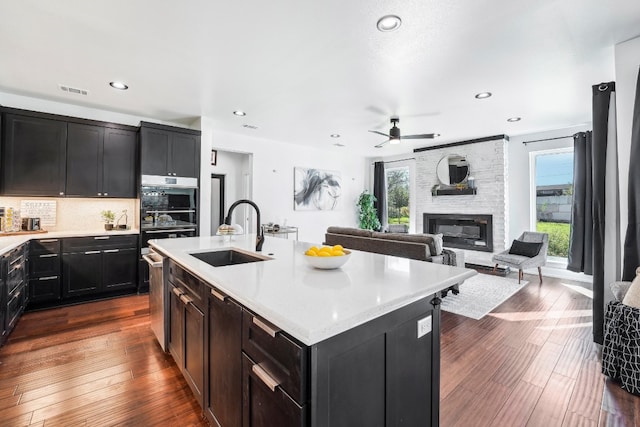 kitchen featuring sink, a center island with sink, dark hardwood / wood-style floors, a fireplace, and backsplash