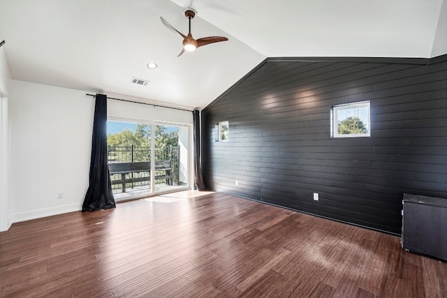 empty room with hardwood / wood-style flooring, ceiling fan, lofted ceiling, and wooden walls