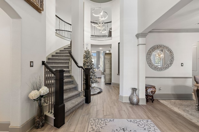 entryway featuring a chandelier, light hardwood / wood-style flooring, crown molding, and ornate columns