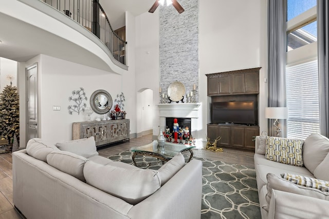 living room featuring ceiling fan, wood-type flooring, a fireplace, and a high ceiling