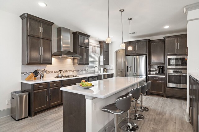 kitchen featuring a center island, light wood-type flooring, wall chimney range hood, and hanging light fixtures