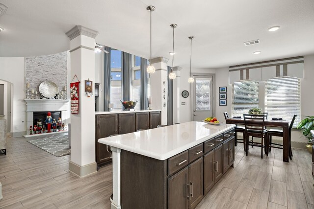 kitchen featuring a large fireplace, a center island, decorative light fixtures, dark brown cabinets, and light wood-type flooring