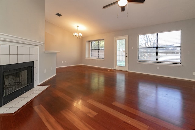 unfurnished living room with ceiling fan with notable chandelier, wood-type flooring, and a tile fireplace