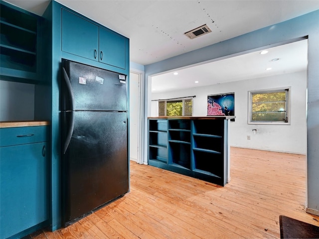 kitchen featuring blue cabinetry, light wood-type flooring, black fridge, and a wealth of natural light