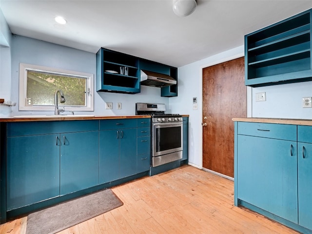 kitchen with wall chimney exhaust hood, blue cabinets, sink, light hardwood / wood-style floors, and stainless steel range with gas stovetop