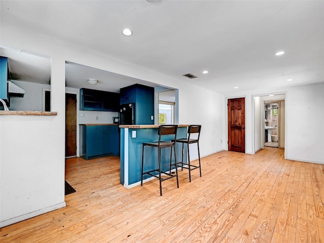 kitchen with blue cabinetry, light wood-type flooring, a kitchen bar, and kitchen peninsula