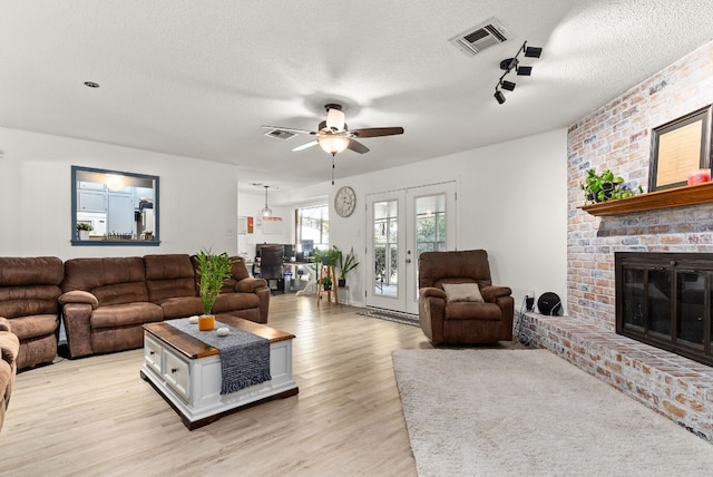 living room featuring ceiling fan, light hardwood / wood-style flooring, a textured ceiling, and a brick fireplace