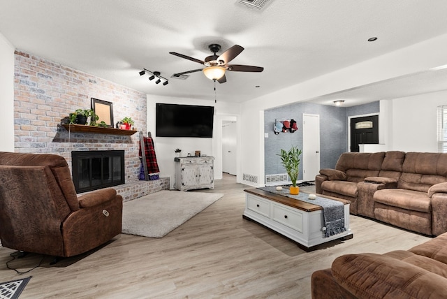 living room featuring ceiling fan, light wood-type flooring, a textured ceiling, and a brick fireplace